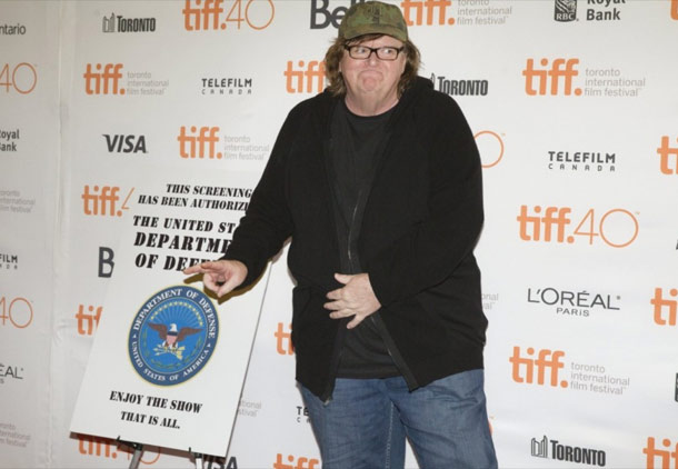 مایکل مور در کنار پوستری که به وزارت دفاع آمریکا می گوید از دیدن فیلم لذت ببرید 